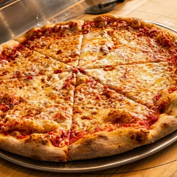 A freshly baked, sliced cheese pizza on a metal pan, resting on a wooden counter.