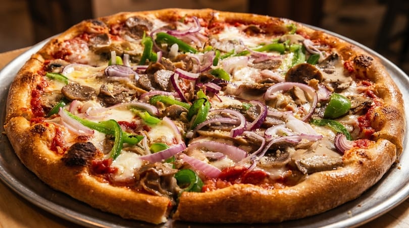 A whole pizza with mushrooms, green peppers, red onions, and cheese on a metal tray.