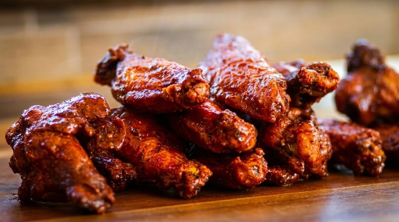 Close-up of a pile of glistening, saucy chicken wings on a wooden surface.